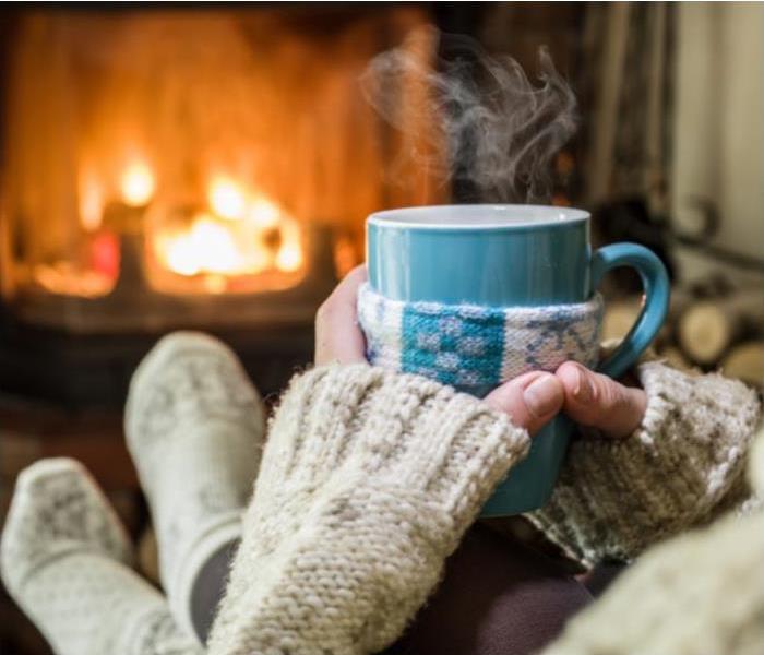 Woman with cocoa and comforter in front of fireplace