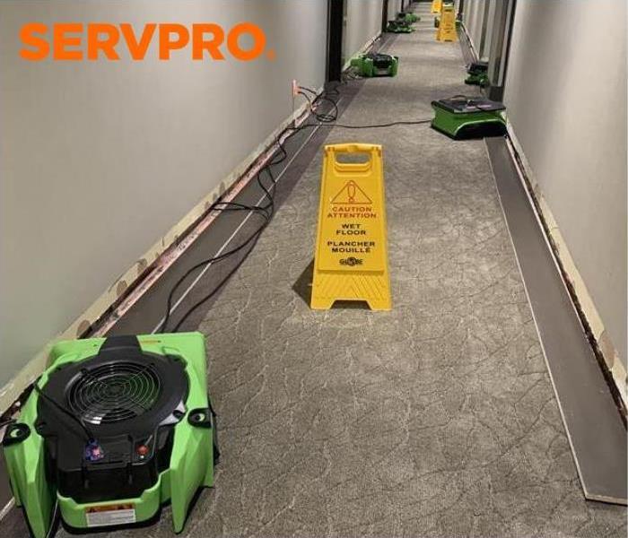 water damage in a flooded hallway with green air movers and yellow caution sign